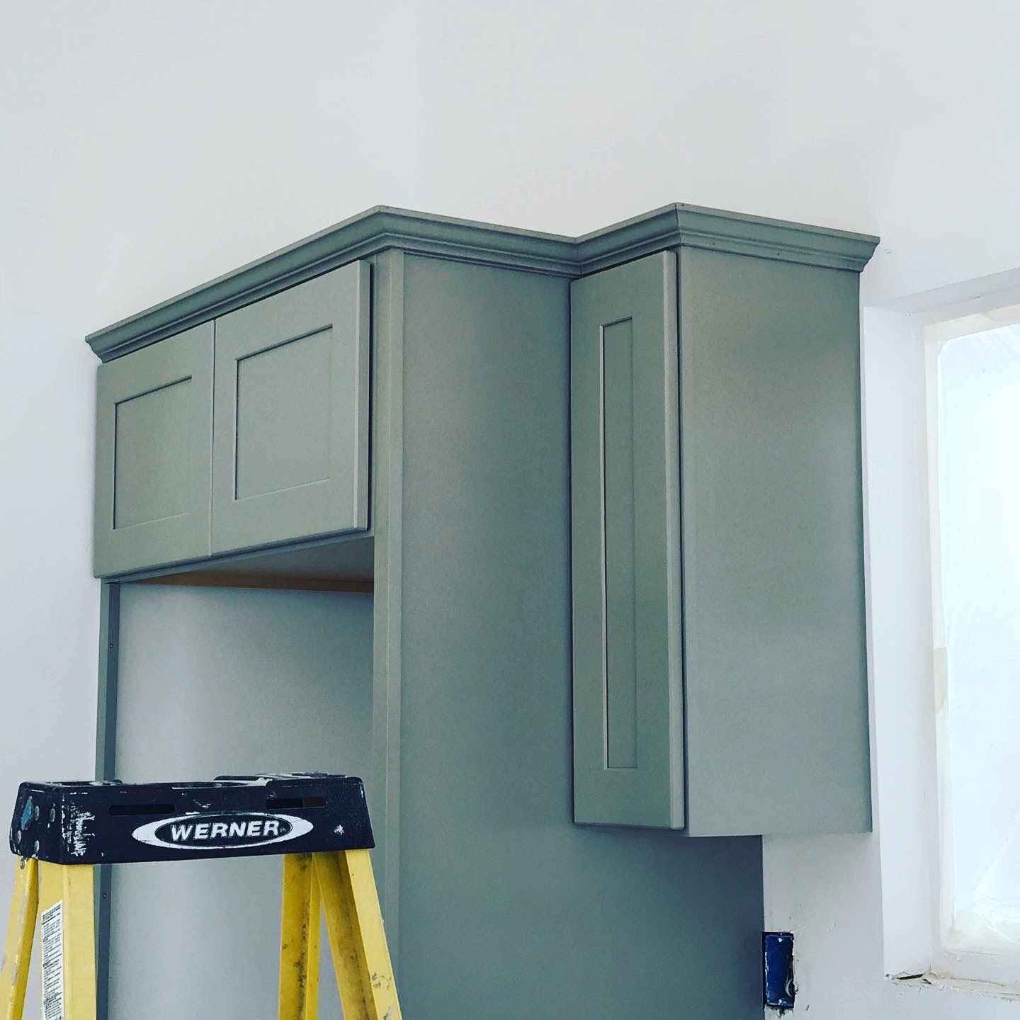 Sage green kitchen upper cabinets with crown molding detail